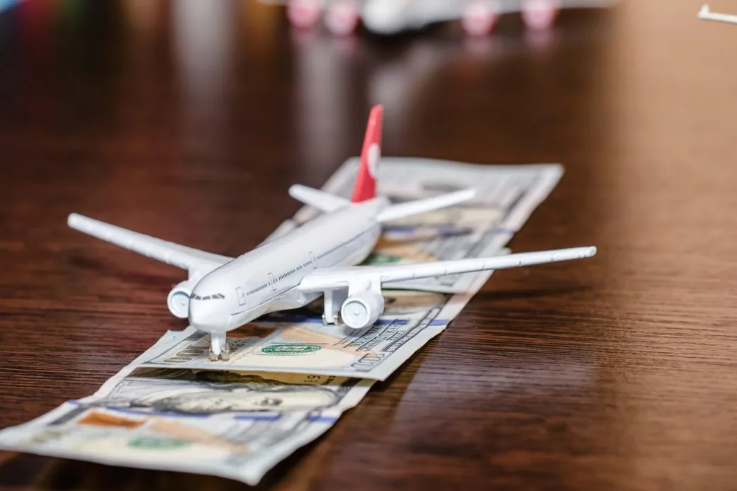 A toy aeroplane resting on top of US dollar banknotes on a wooden table.