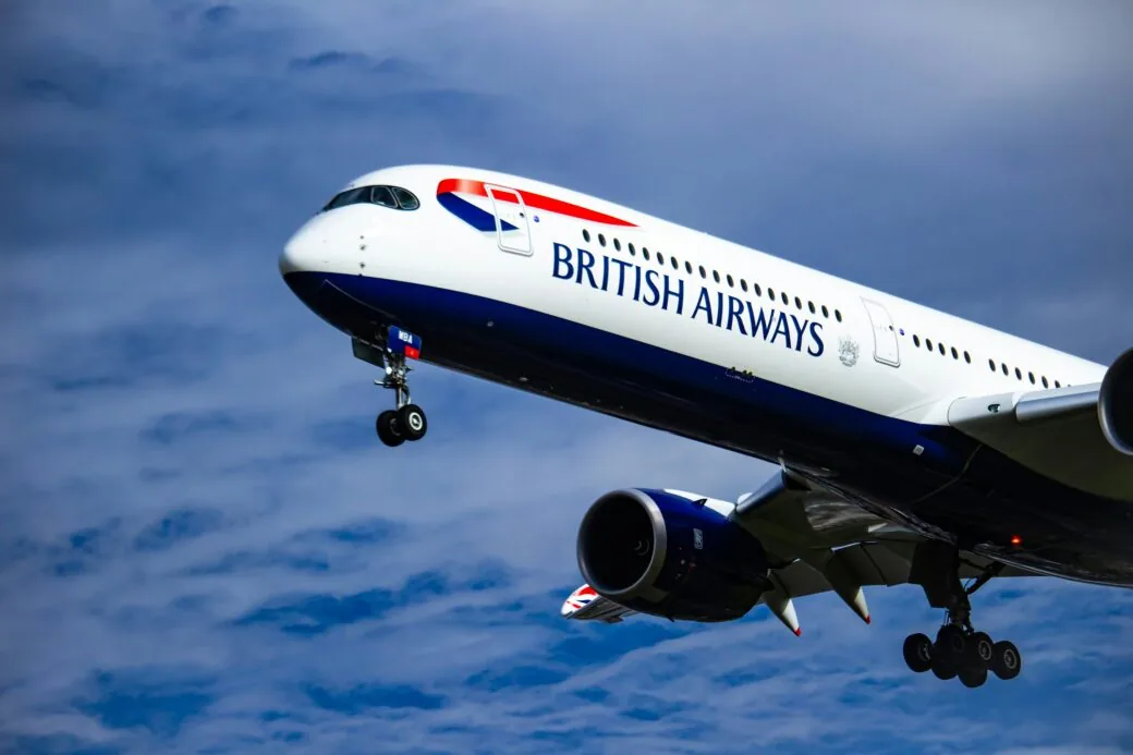 A British Airways aircraft climbing after take-off against a cloudy blue sky.