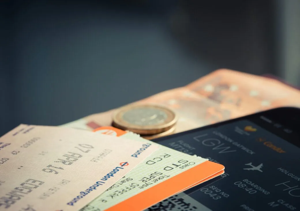 Travel tickets, a coin and a phone showing a boarding pass laid out together.