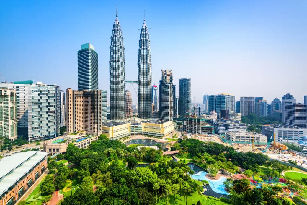 The Petronas Towers rising above the Kuala Lumpur skyline with parkland in the foreground.