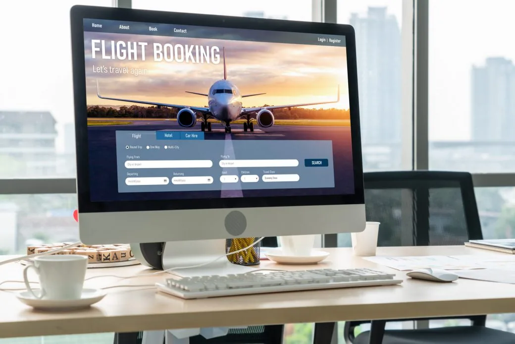 A desktop monitor displaying a flight booking website homepage on an office desk.