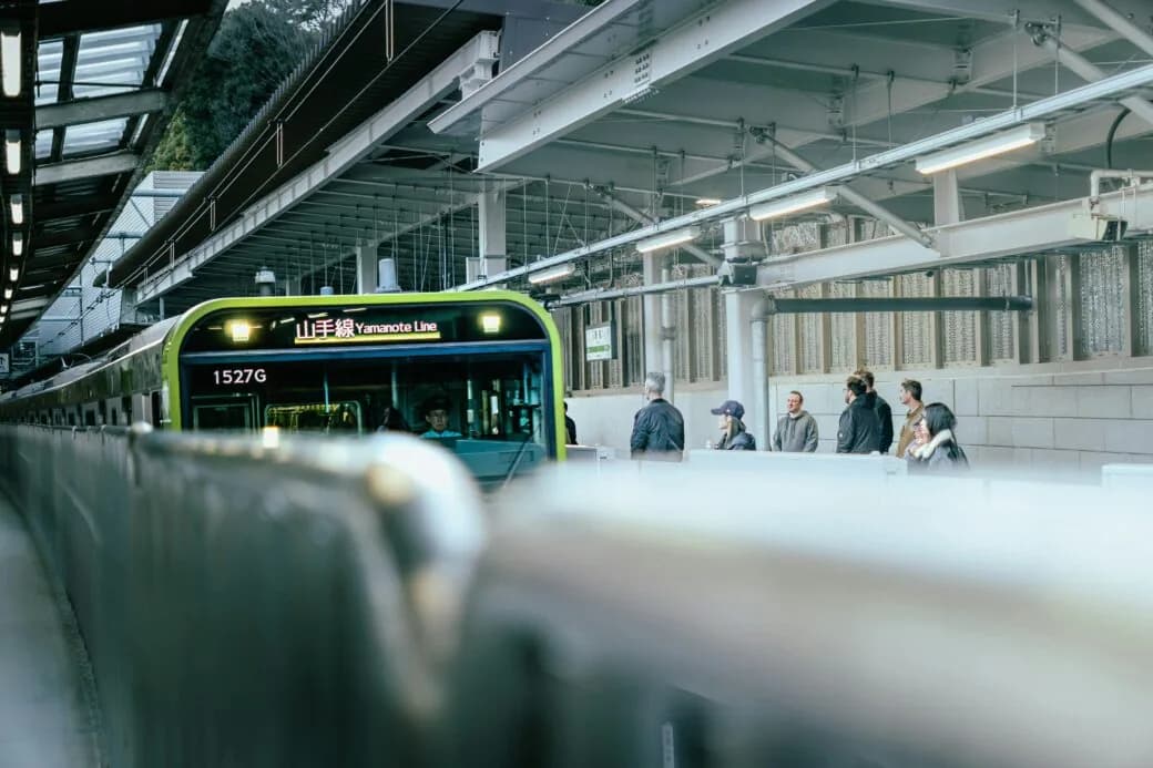 Passengers wait on a station platform as a Yamanote Line train pulls in.
